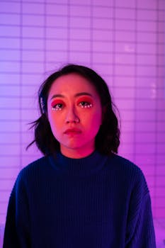 Portrait of a young woman with artistic eye makeup against a tiled background in vibrant lighting.