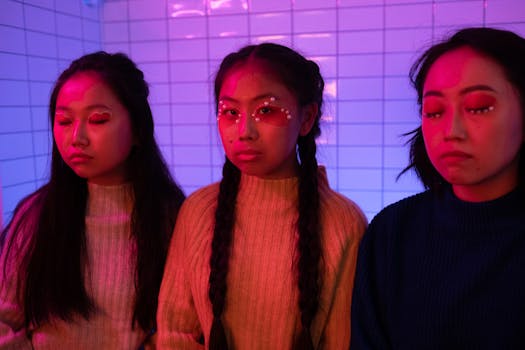 Three women with artistic makeup pose in vibrant lighting wearing cozy knitwear.