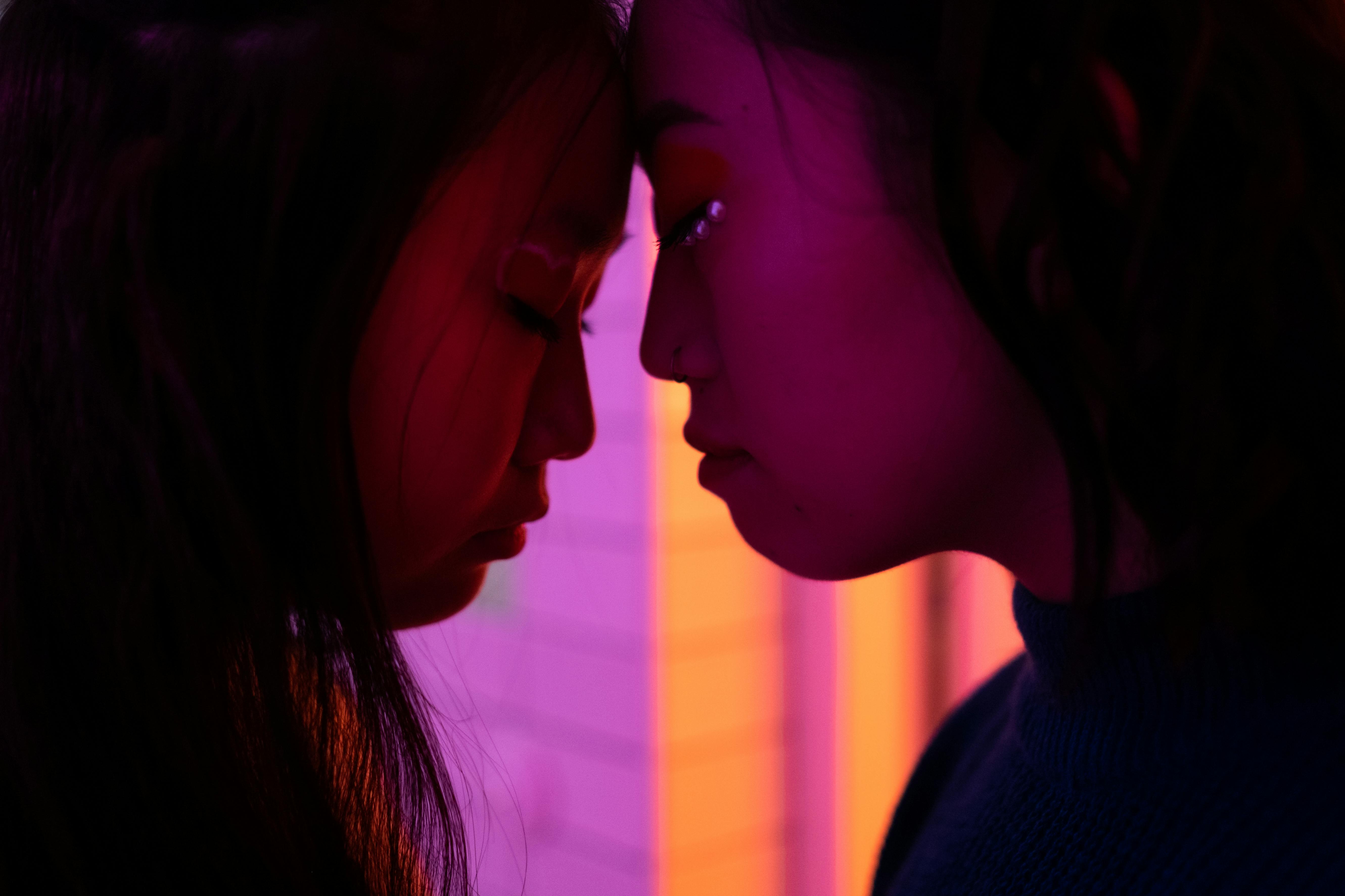 Intimate profile of two women touching foreheads bathed in vibrant neon light.