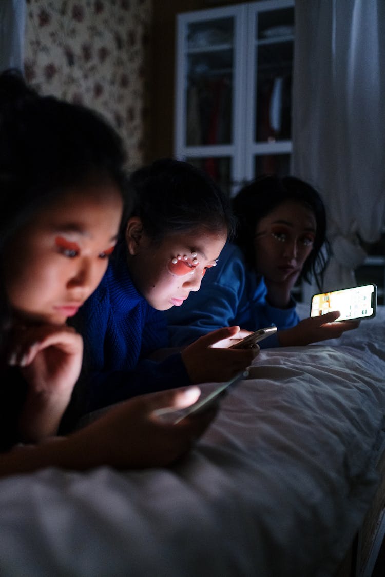 Friends Lying On Bed While Using Phones At Night