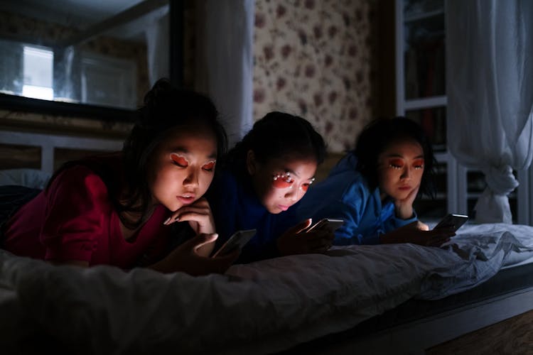 Women Lying Down On The Bed While Using Their Smartphones 