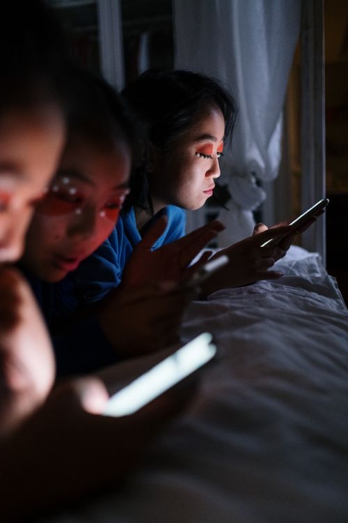 Free Three teenagers using smartphones in a dimly lit bedroom at night, focusing on screens. Stock Photo