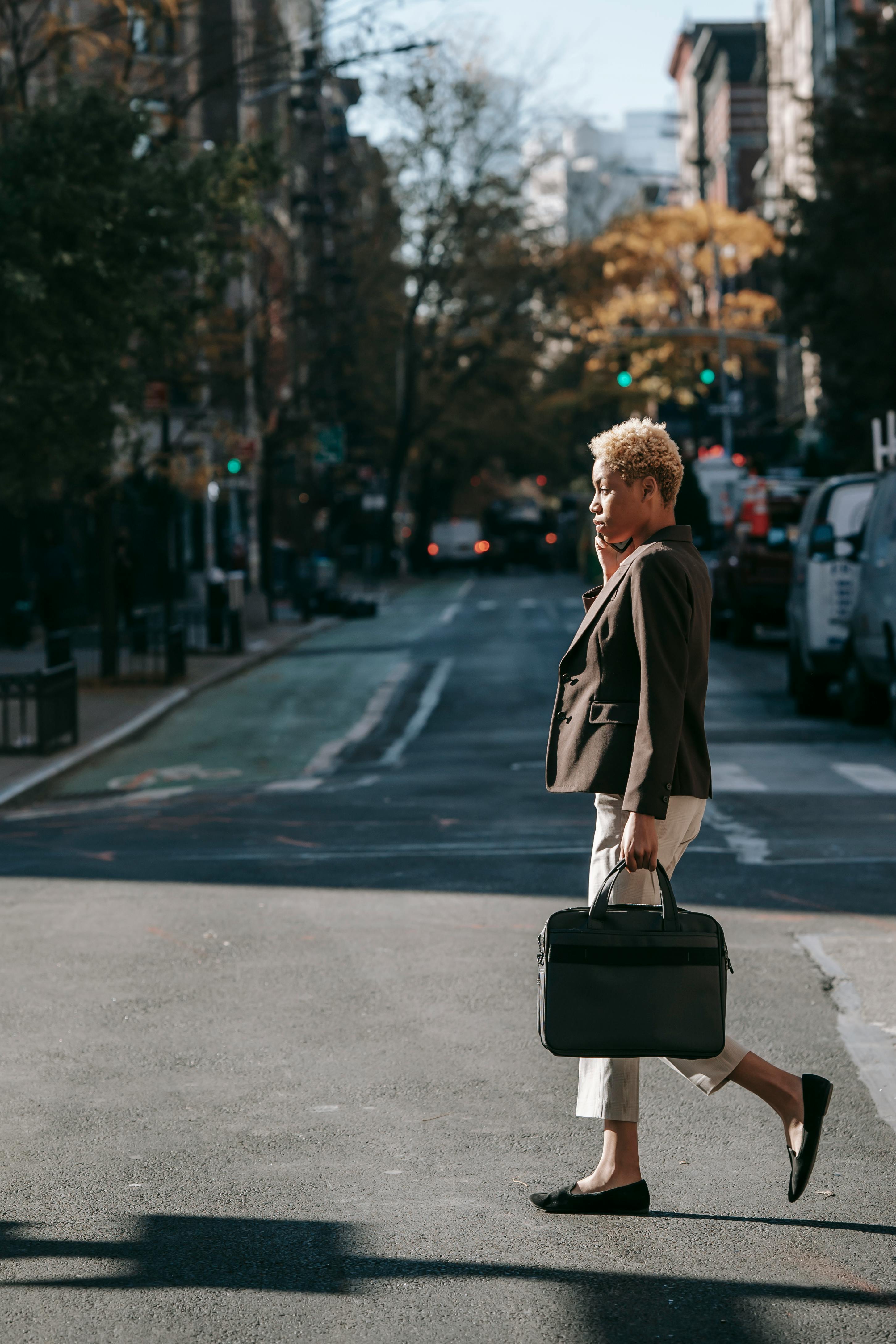 focused young ethnic female crossing road and talking on smartphone