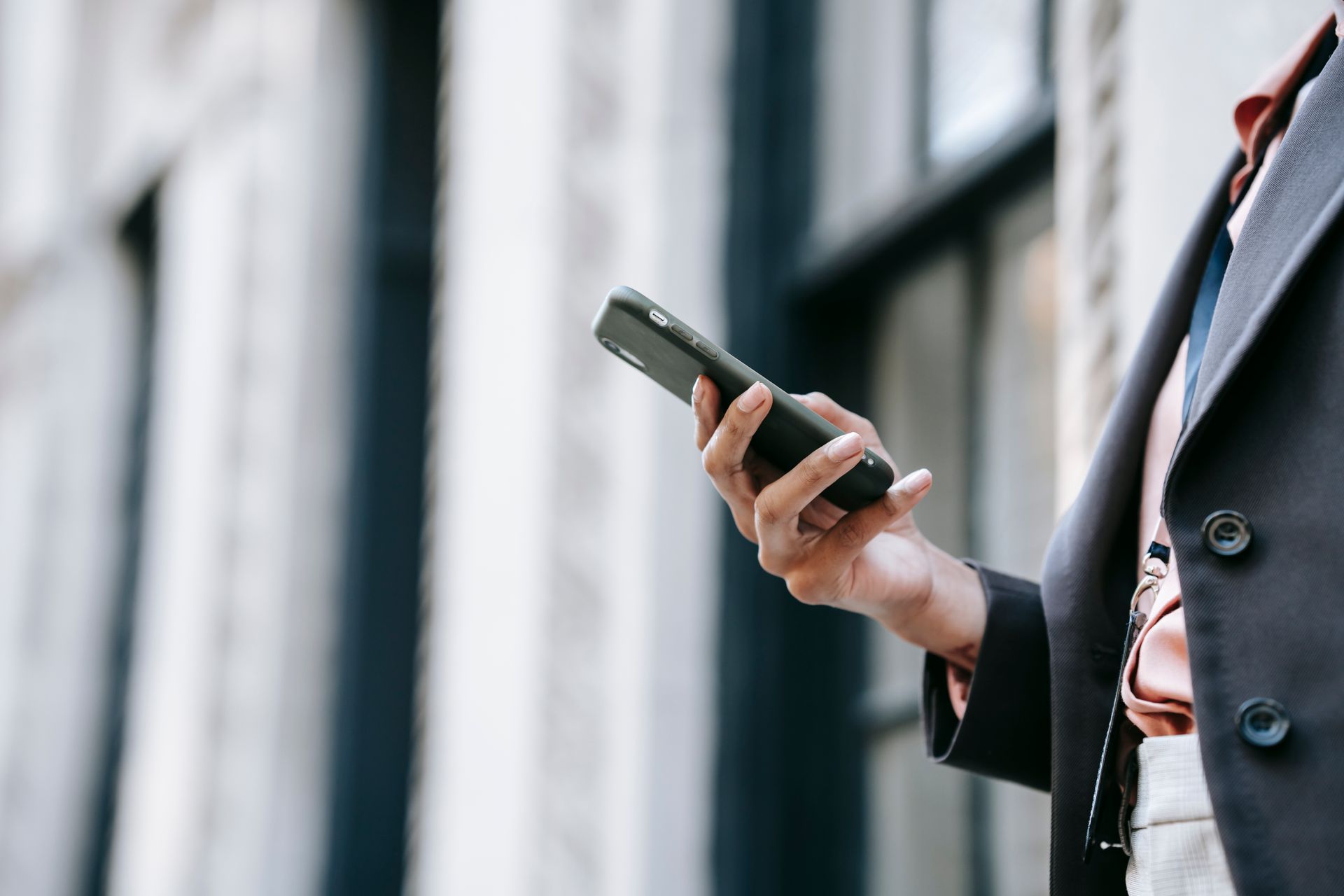 Side view of crop unrecognizable female manager in stylish outfit using mobile phone while standing on street near building before going to work