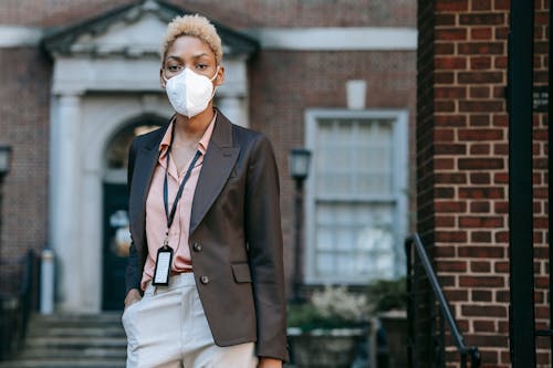 Free Serious young black female entrepreneur with short dyed hair in stylish suit and protective mask standing on street near brick building with had in pocket and looking at camera Stock Photo