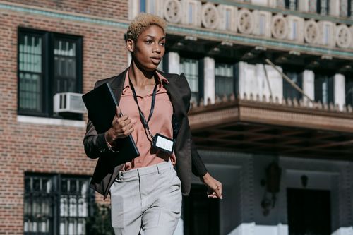 Free Confident African American female entrepreneur in classy outfit with badge carrying laptop while running fast on street Stock Photo