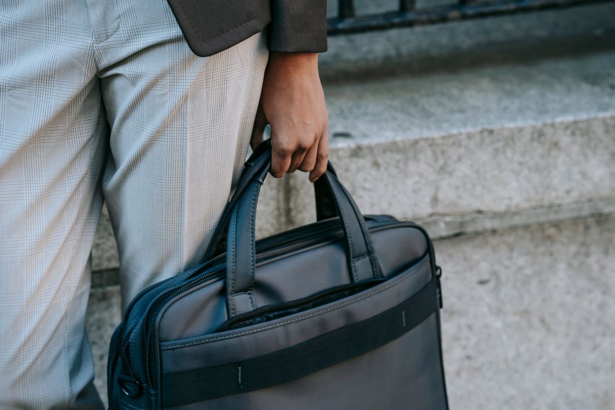 Crop anonymous person in stylish outfit carrying laptop in bag while walking along street Illustrative editorial photograph.