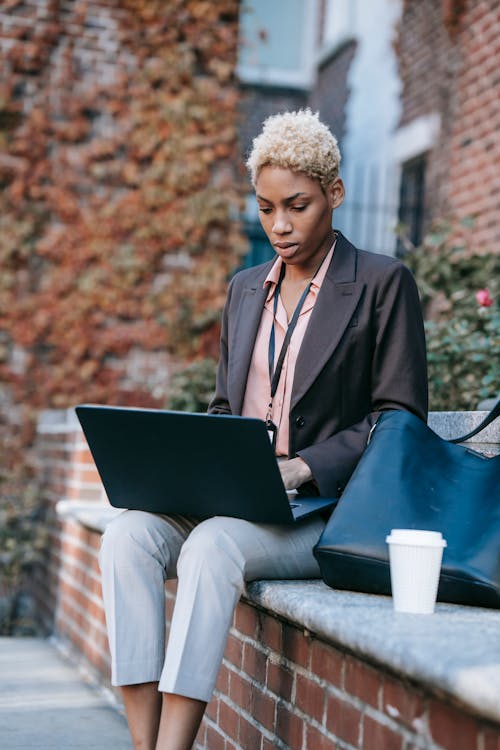 Mujer En Chaqueta Negra Sentada En Un Banco Gris Con Laptop