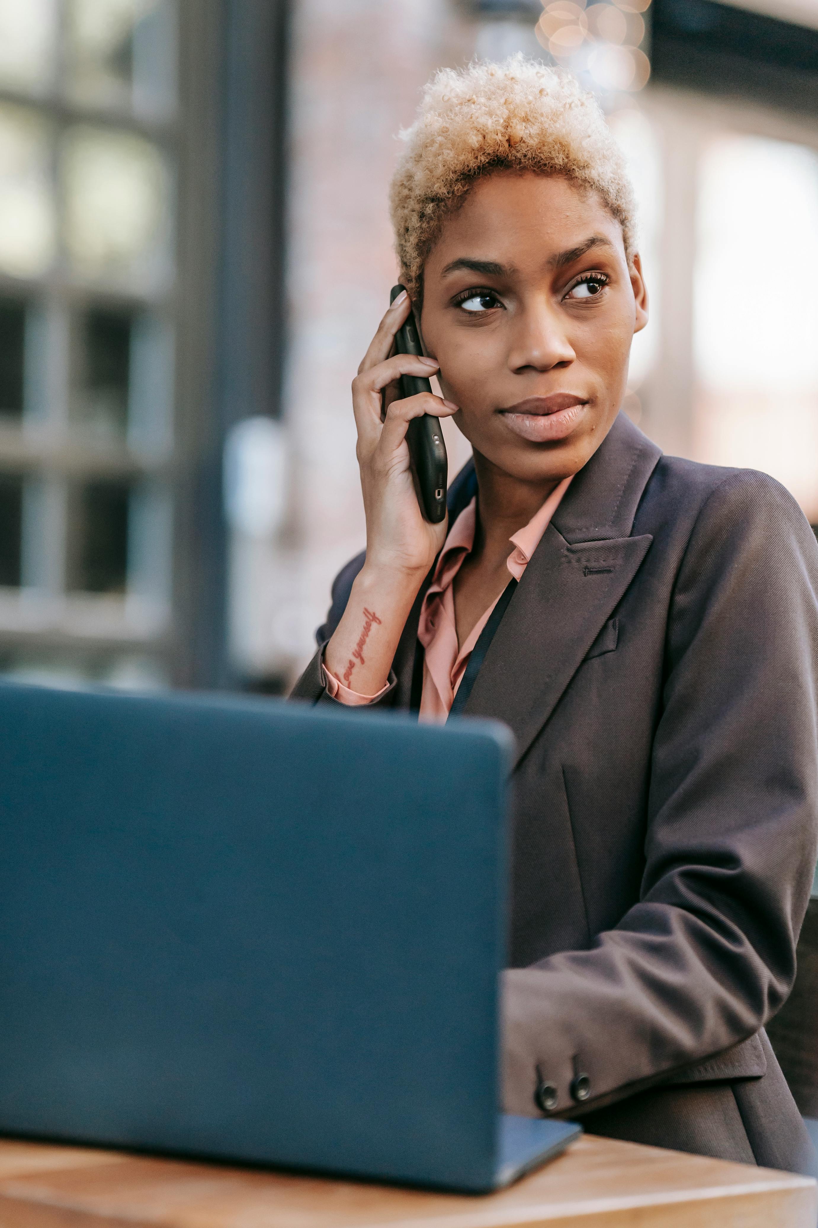 black woman talking on smartphone and browsing laptop for work