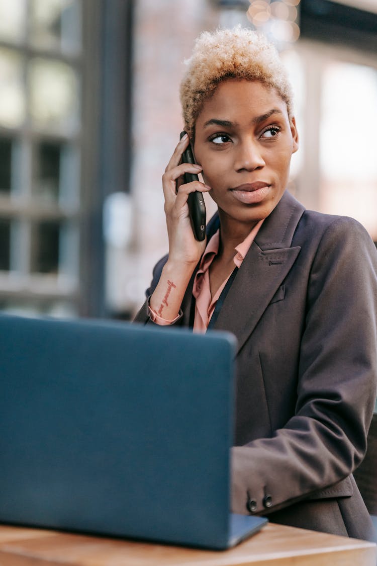 Black Woman Talking On Smartphone And Browsing Laptop For Work