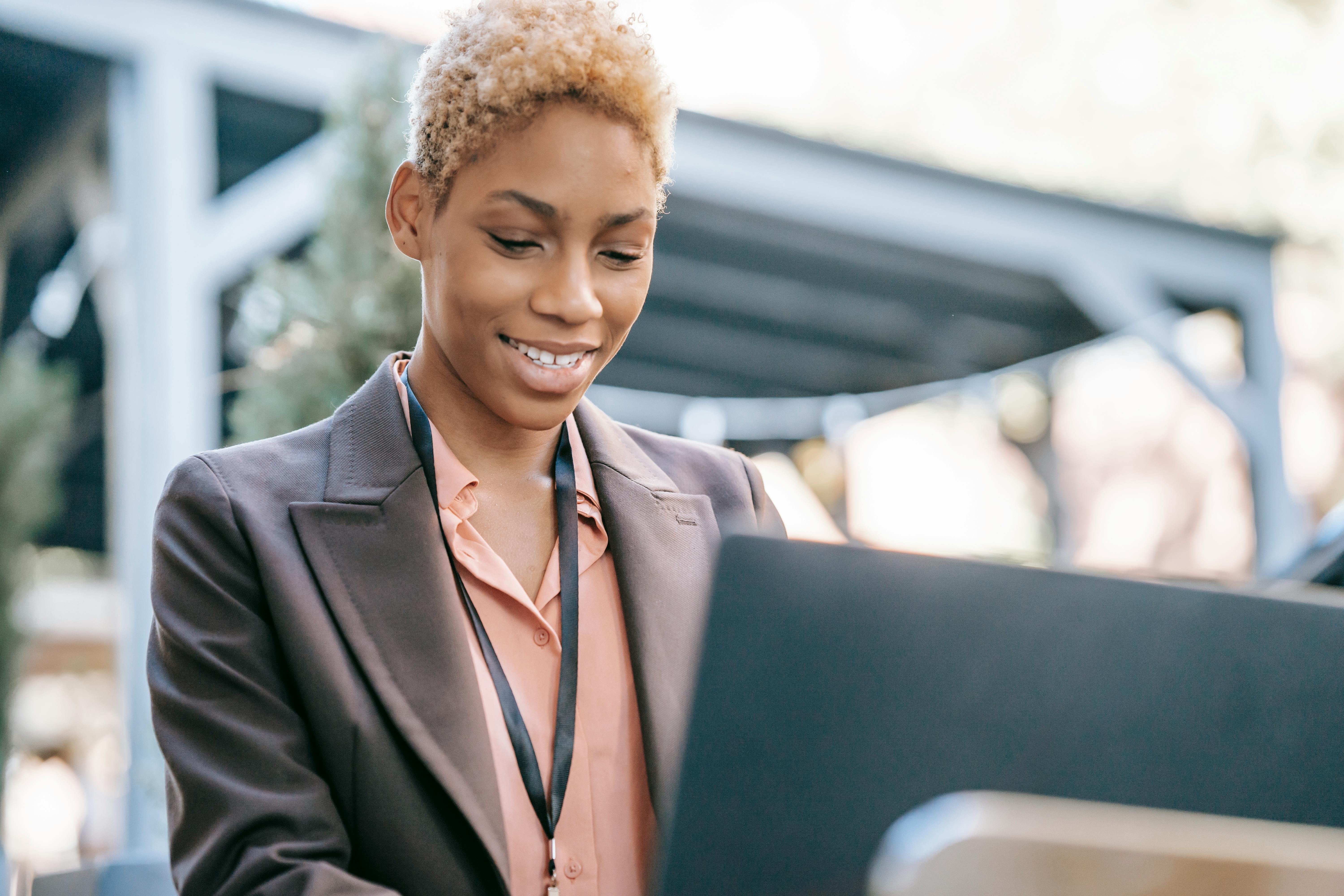 Empreendedorismo Digital: Como a tecnologia transforma negócios 2 Smiling young woman in a suit using a laptop outdoors, demonstrating professional confidence.