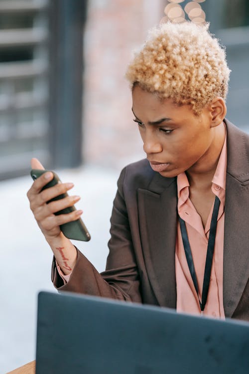 Focused African American female executive watching mobile phone while working on business project remotely