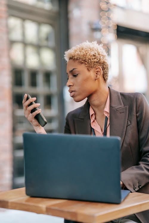 Serious black female entrepreneur watching smartphone and using laptop