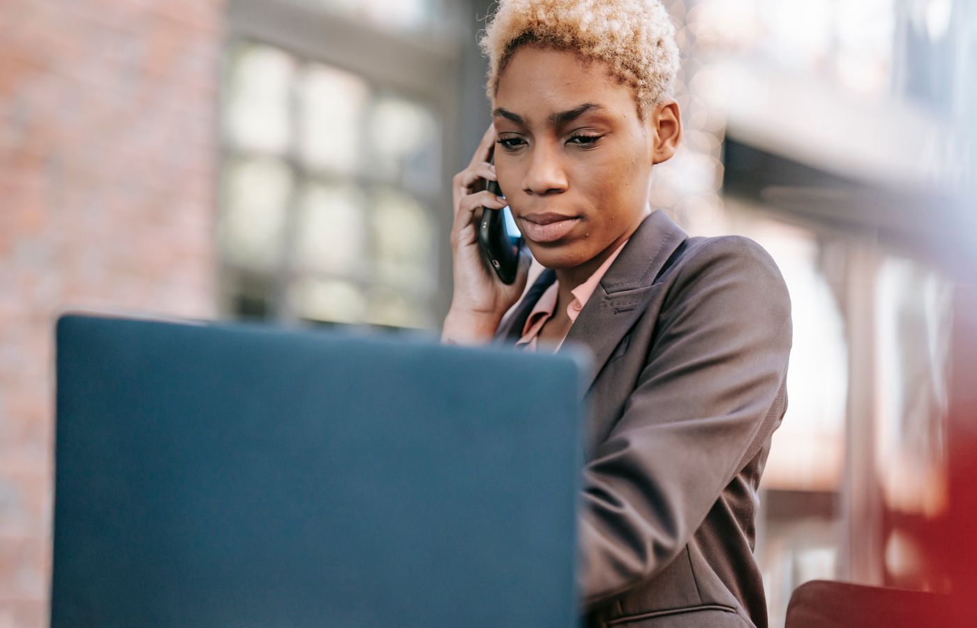 Focused professional woman multitasking using a laptop and phone outdoors.
