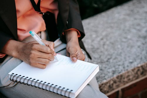 Free From above of crop anonymous ethnic woman making list in notebook during work in park Stock Photo