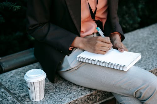 Ethnic woman writing notes in planner with takeaway coffee