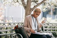 Pensive young African American female student in stylish jacket reading documents in folder and eating sandwich sitting in park