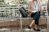 Crop unrecognizable female student reading papers in folder while eating sandwich on bench in park