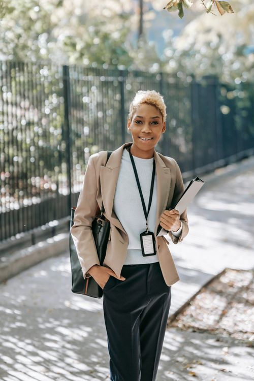 Free Smiling young African American female entrepreneur in formal jacket with folder and handbag looking at camera Stock Photo