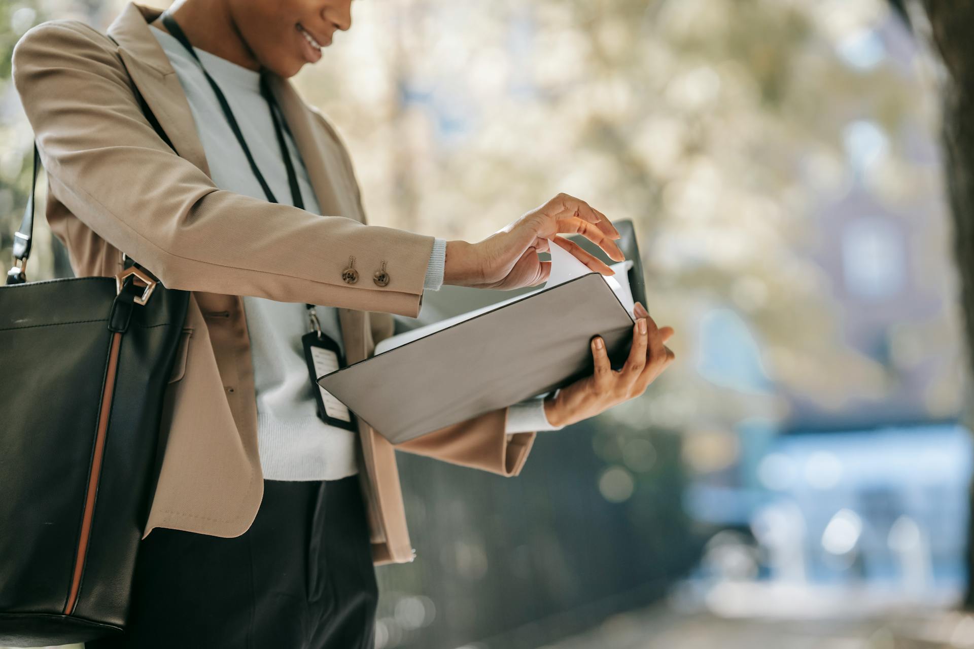 Elegant businesswoman checks documents in a folder while standing outdoors in a modern setting.