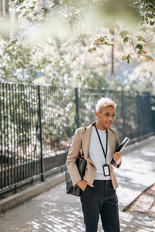 Free Cheerful young African American female entrepreneur standing near metal fence with papers in folder and looking away Stock Photo