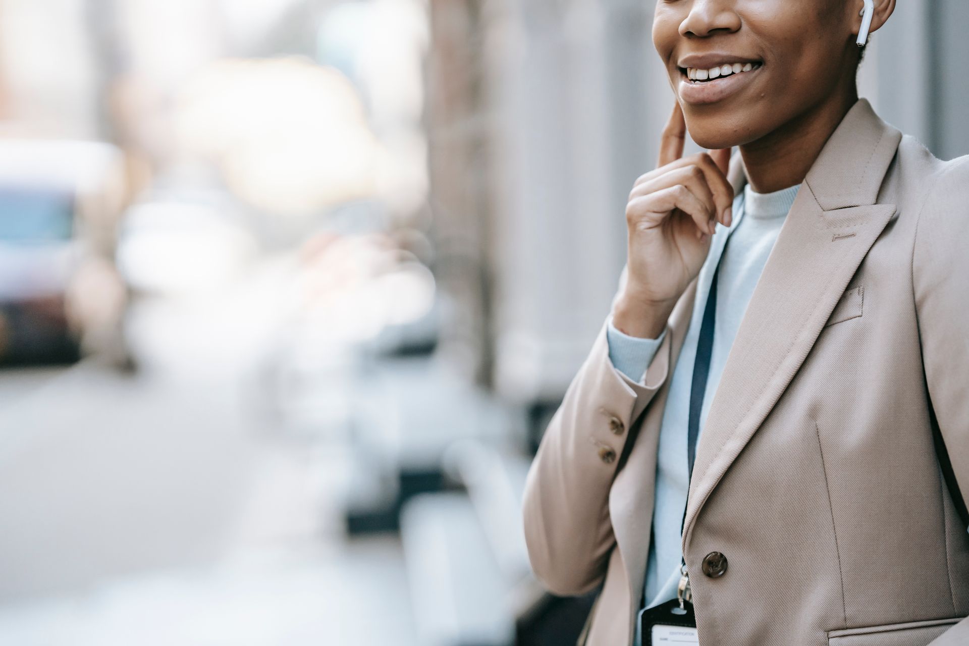 Happy woman in a beige jacket enjoying music through wireless earbuds on a city street.