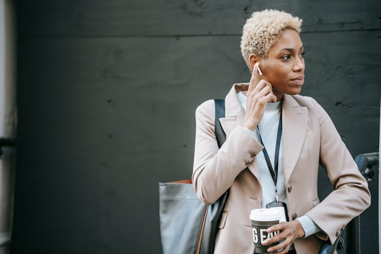 Contemplative Ethnic Office Employee With Earphone And Takeaway Coffee Outdoors