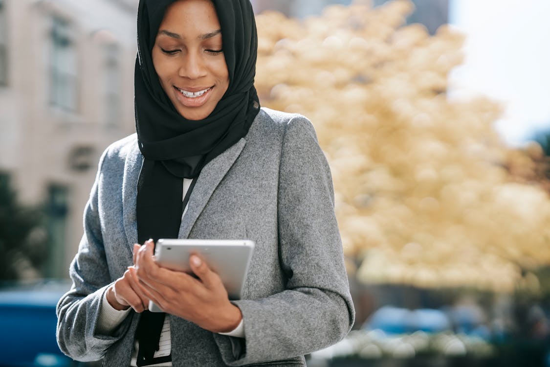 Free Happy Crop Young African American Lady In Elegant Suit And Traditional Hijab Smiling While Browsing Tablet On City Street Stock Photo