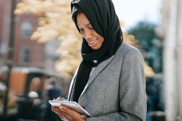 Happy Young Black Female Manager In Hijab Using Tablet On Street