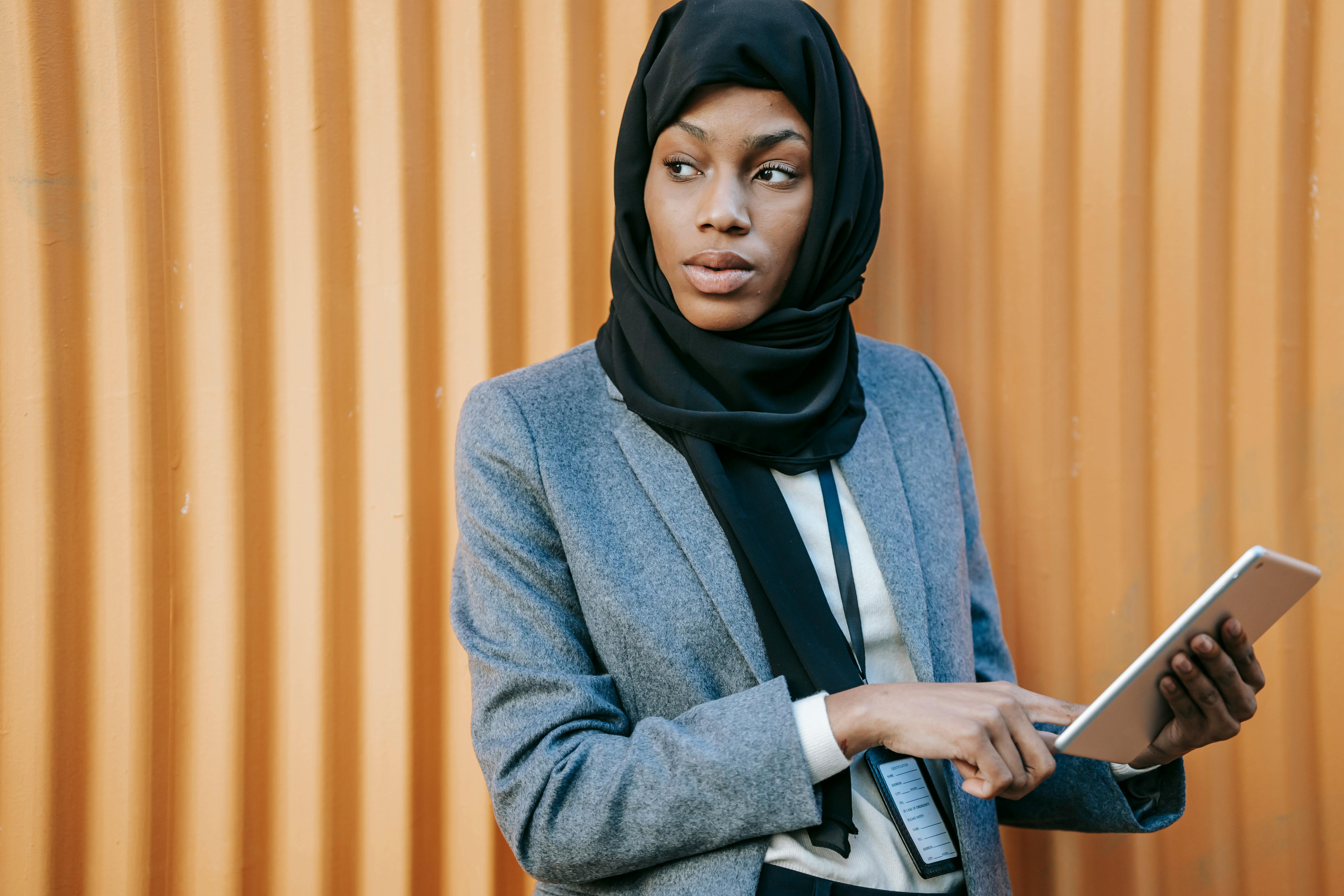 Empreendedorismo Digital: Como a tecnologia transforma negócios 4 Concentrated young African American female employee in elegant suit and traditional hijab working on tablet and looking away on street