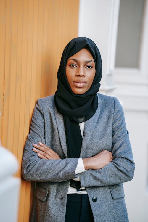 Free Confident young African American businesswoman in stylish suit and Islamic headscarf standing near wall with crossed arms and looking at camera Stock Photo