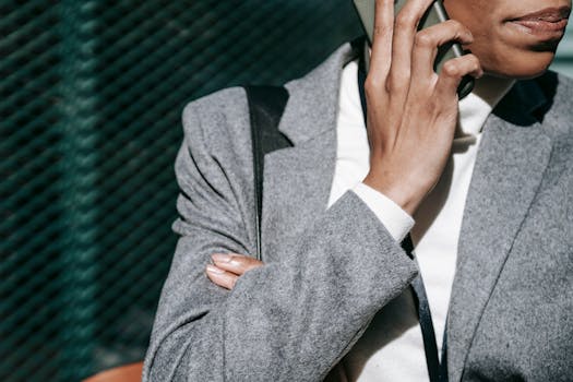 Businesswoman in grey suit talking on smartphone outdoors with blurred urban background.