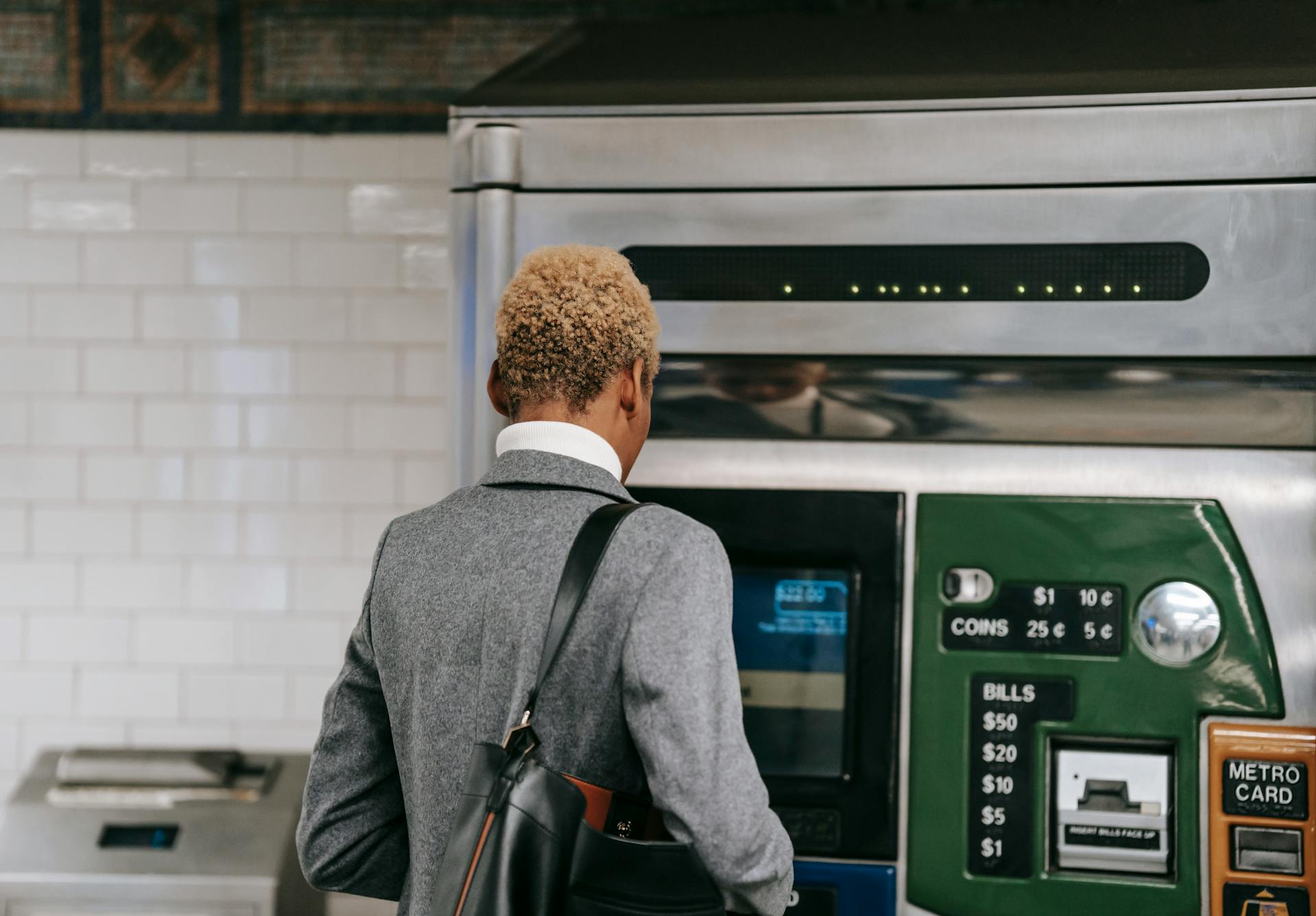 Back view of unrecognizable ethnic female manager with short dyed hair in elegant suit buying ticket with electronic machine in subway station