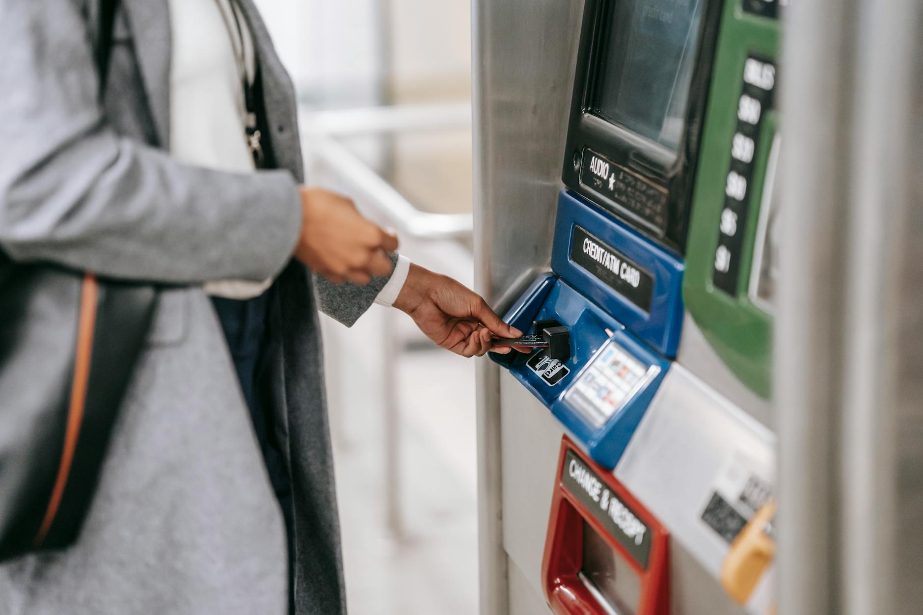 Side view of crop unrecognizable female in stylish clothes using credit card while buying metro ticket via electronic machine