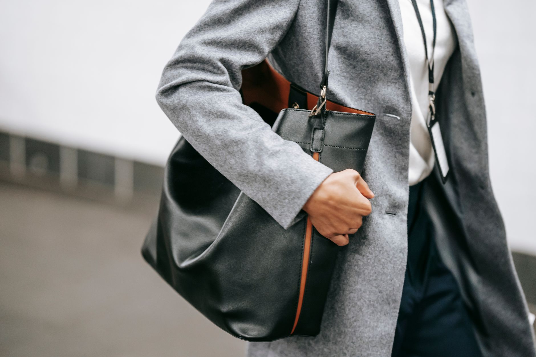 Crop faceless female entrepreneur in stylish classy outfit with bag and name tag walking on city street
