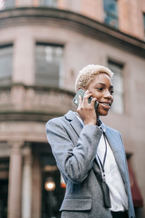 Free Positive young African American female entrepreneur in gray jacket having phone call standing on street near building and looking away Stock Photo