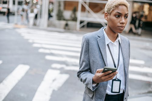 Serious black businesswoman with smartphone near road