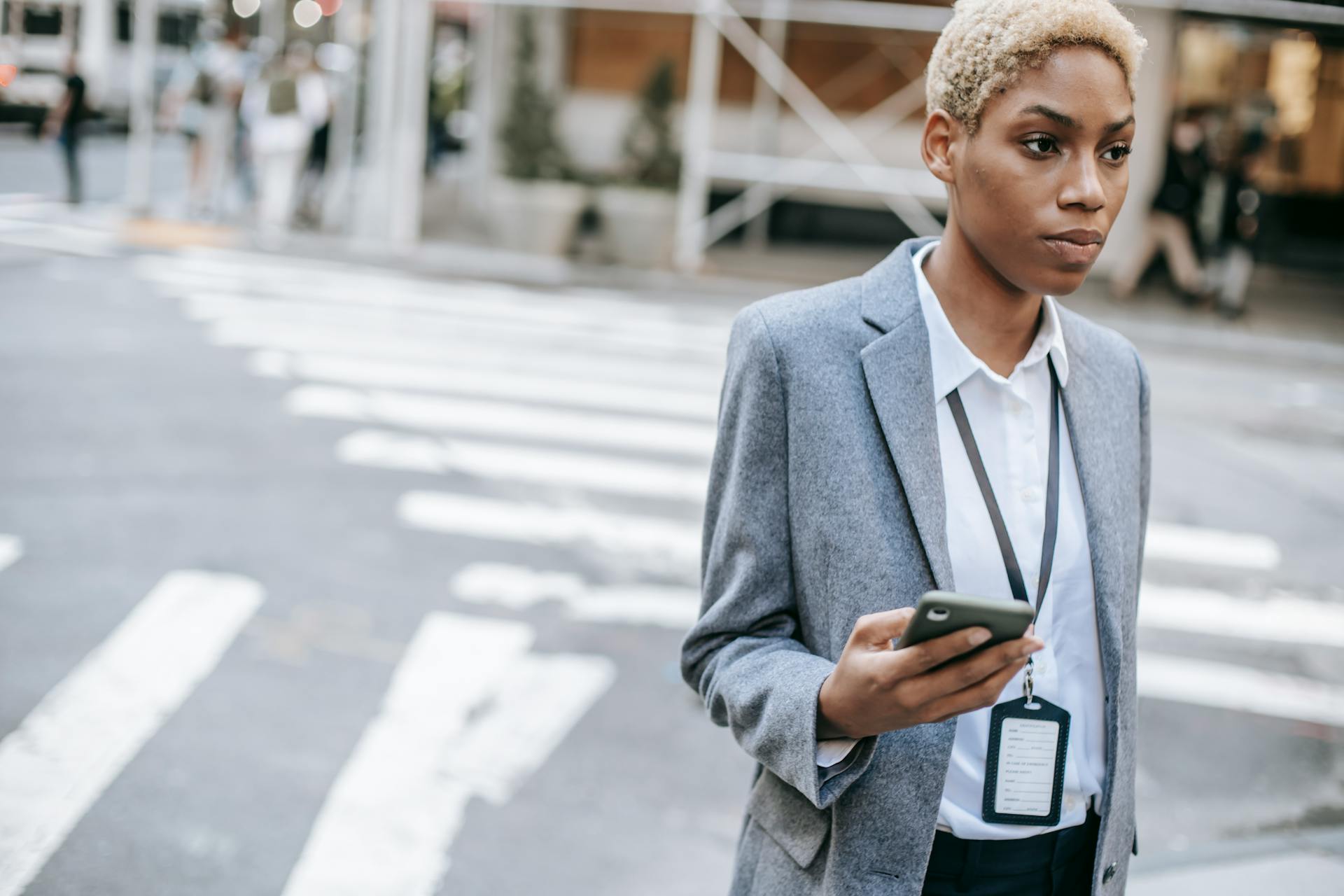 Young African American businesswoman using cellphone at a crosswalk in the city, depicting modern urban life.