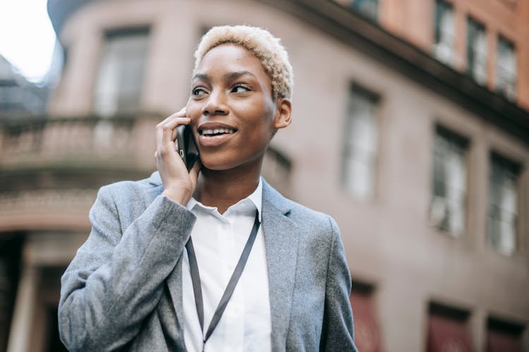 Delighted Black Businesswoman Speaking Via Smartphone In City Street