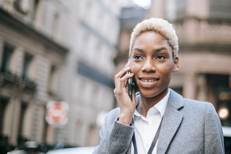 Positive Black Lady Speaking Via Modern Smartphone On City Street