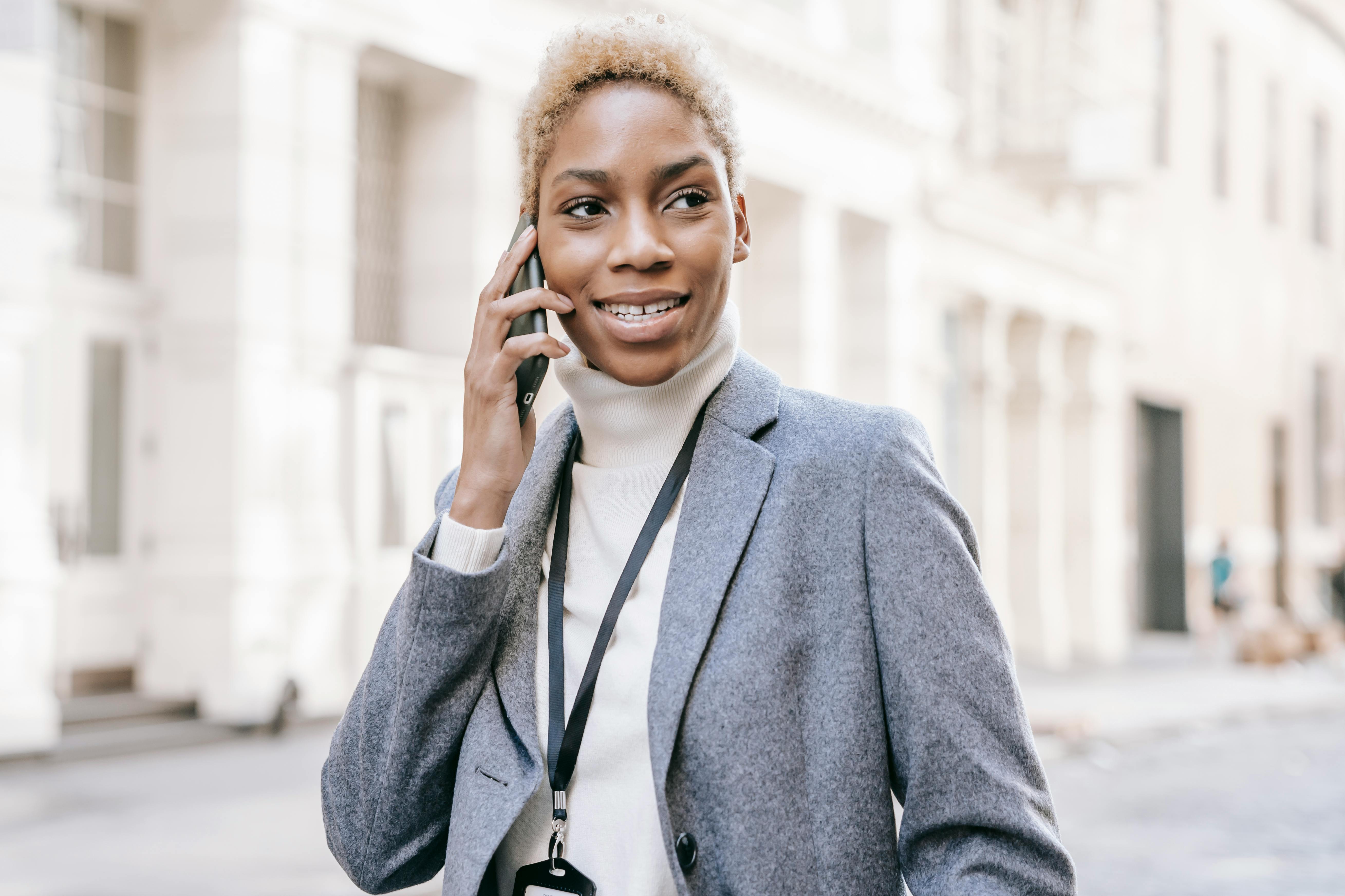 delighted black lady smiling while talking on mobile phone on city street