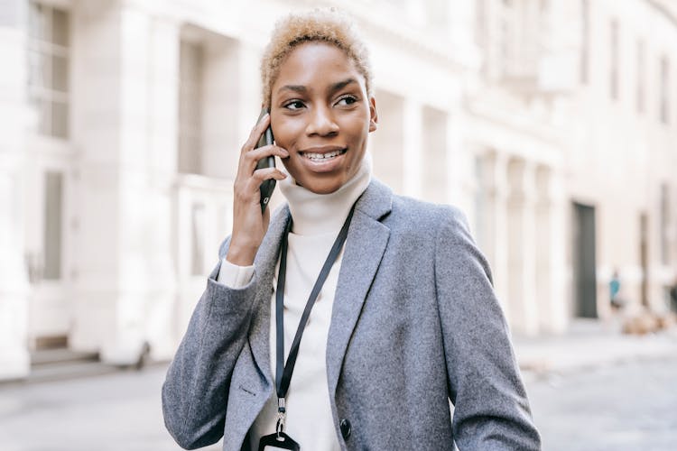 Delighted Black Lady Smiling While Talking On Mobile Phone On City Street