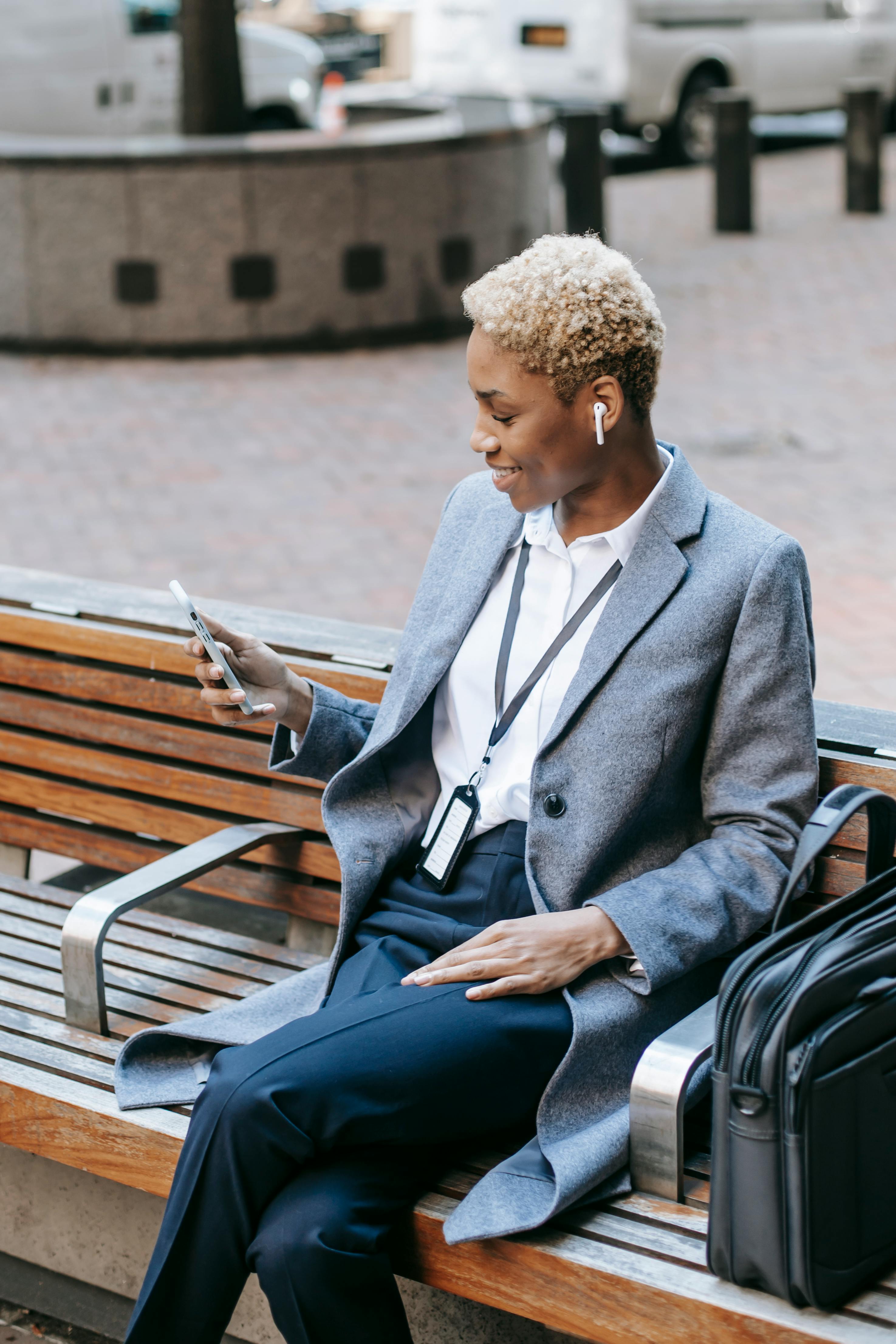 happy black female using modern smartphone while sitting on bench in megapolis street