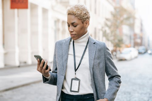 Confident young  African American lady with badge around neck standing on pavement and watching video on smartphone in daylight