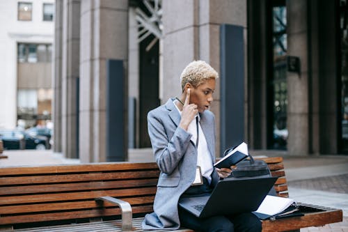 Free Concentrated self employed female entrepreneur working remotely while sitting with laptop and papers near urban building in daytime Stock Photo