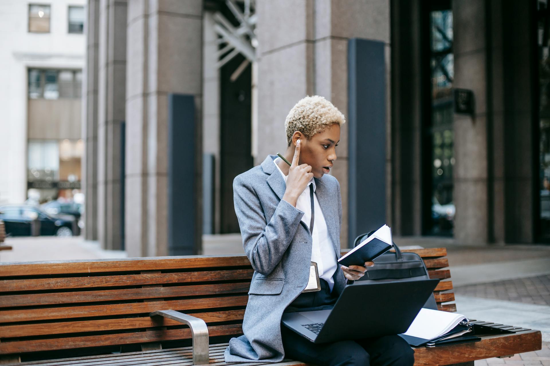 Concentrated self employed female entrepreneur working remotely while sitting with laptop and papers near urban building in daytime