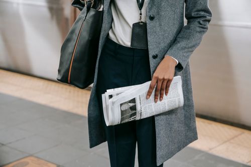 Free From above of crop anonymous female employee in elegant outfit and name tag standing on platform of metro station with newspaper in hand Stock Photo