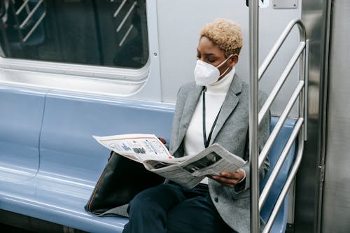 Free Serious black lady in medical mask reading newspaper in train Stock Photo