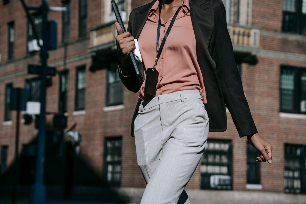 A Black woman walking through the city in a tailored coat, laptop in hand — Adaeze, for BossBabe Gangster (bossbabegangster.com)