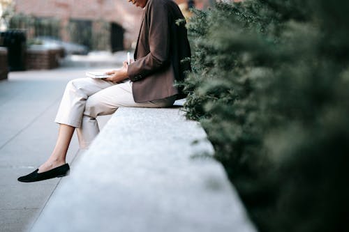 黑色長袖襯衫和白色的褲子，坐在混凝土長凳上的女人